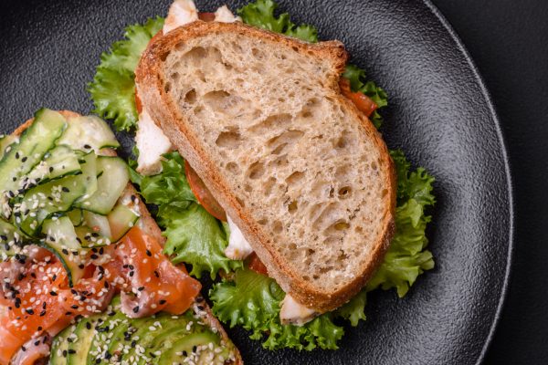 Fresh tasty sandwich with salmon, avocado and sesame and flax seeds on a dark concrete background